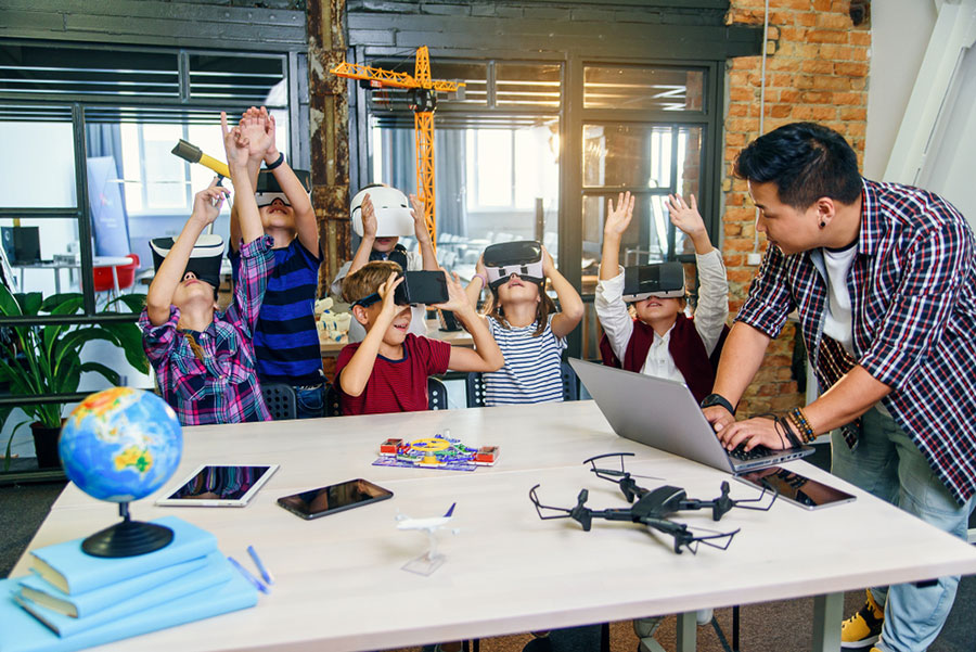 Un professeur et des enfants avec un ordinateur et des casques de réalité virtuelle.